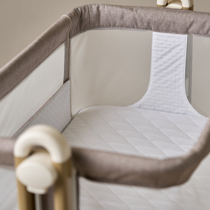 Bedside crib with taupe woven fabric, mesh sides, quilted white mattress