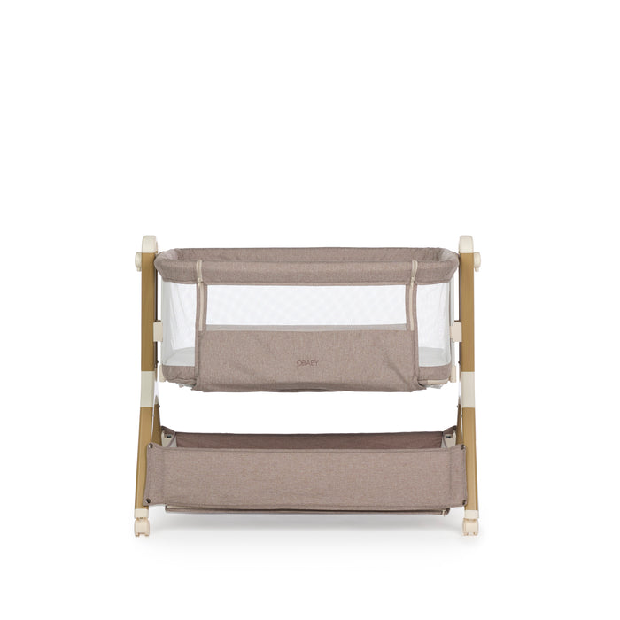 Bedside crib with taupe woven fabric, mesh sides, zipped up parent window, wood effect frame with ivory plastics & wheels. Storage basket underneath.