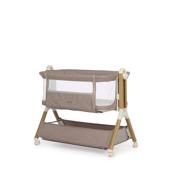 Bedside crib with taupe woven fabric, mesh sides, zipped up parent window, wood effect frame with ivory plastics & wheels. Storage basket underneath.