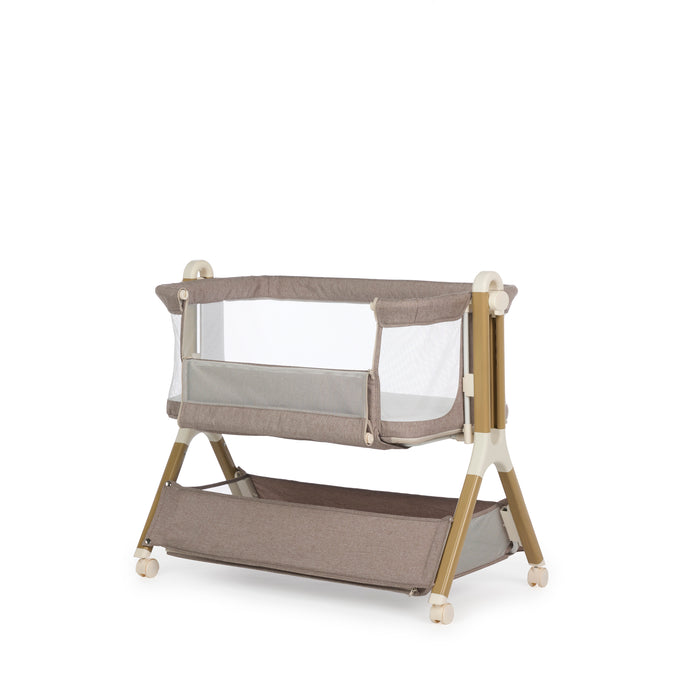 Bedside crib with taupe woven fabric, mesh sides, unzipped  parent window, wood effect frame with ivory plastics & wheels. Storage basket underneath.