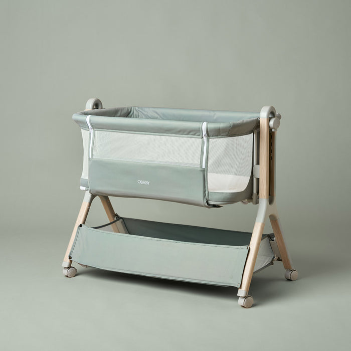 bedside crib with sage green fabric, wood effect frame, mesh windows on all 4 sides, zip up parent panel, allowing easy access to baby.