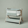 bedside crib with sage green fabric, wood effect frame, mesh windows on all 4 sides, zip up parent panel, allowing easy access to baby.