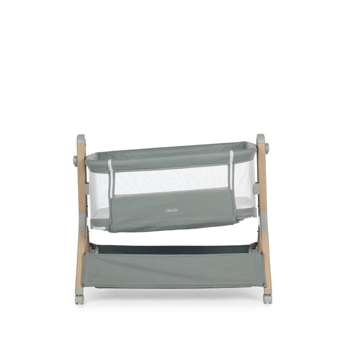 Bedside Crib, sage with wood effect frame , grey plastics & grey wheels, showing the crib mounted on a tilt to help babies with colic.