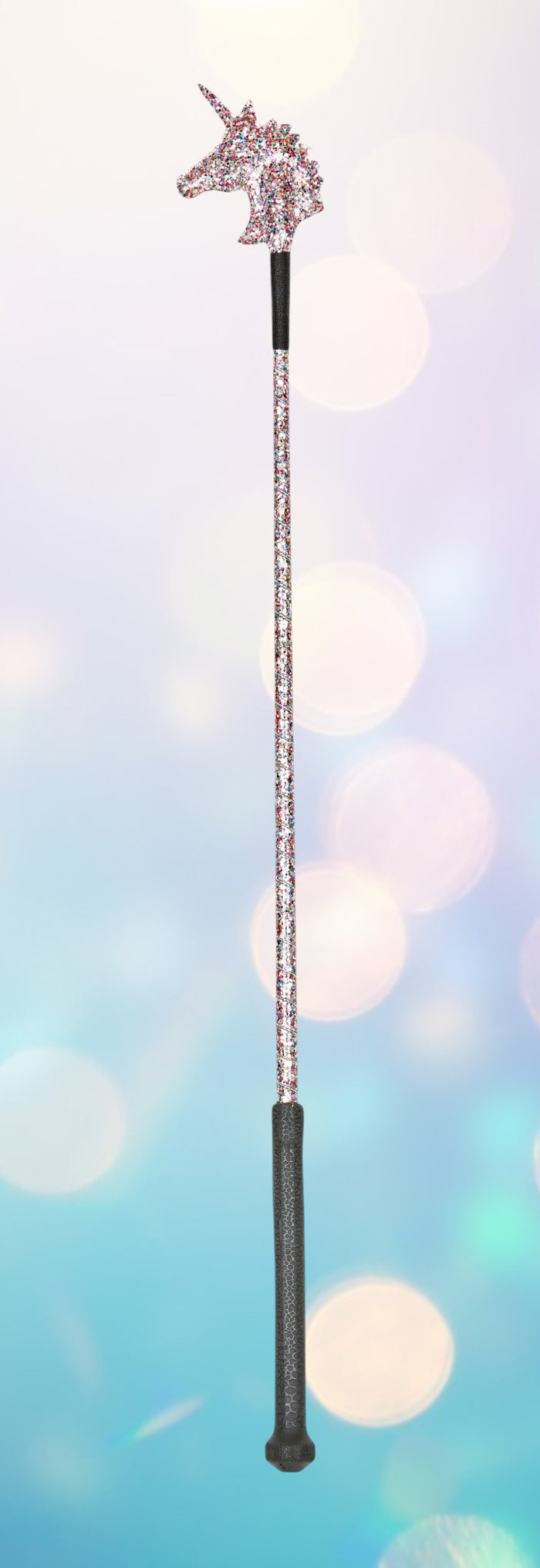 A unicorn-themed riding crop with a sparkly unicorn head at the top, a long sparkly shaft, and a dark textured handle, shown against a soft pastel bokeh background.