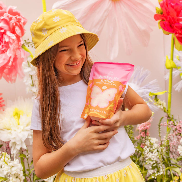 Young girl in a yellow hat and skirt holding a pink and orange package amidst flowers